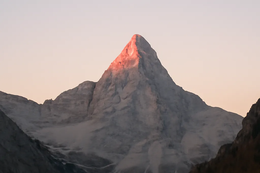 Sommet calcaire en pyramide des Alpes juliennes éclairé de rose au lever du soleil, au-dessus d’une vallée glaciaire
